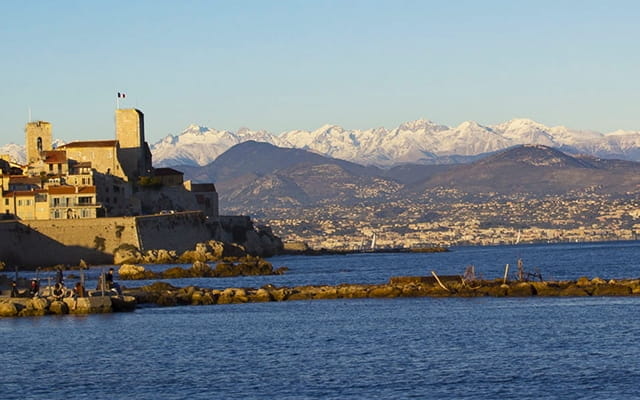 Vue de la ville d'Antibes depuis la mer donnant sur des monts enneigés.