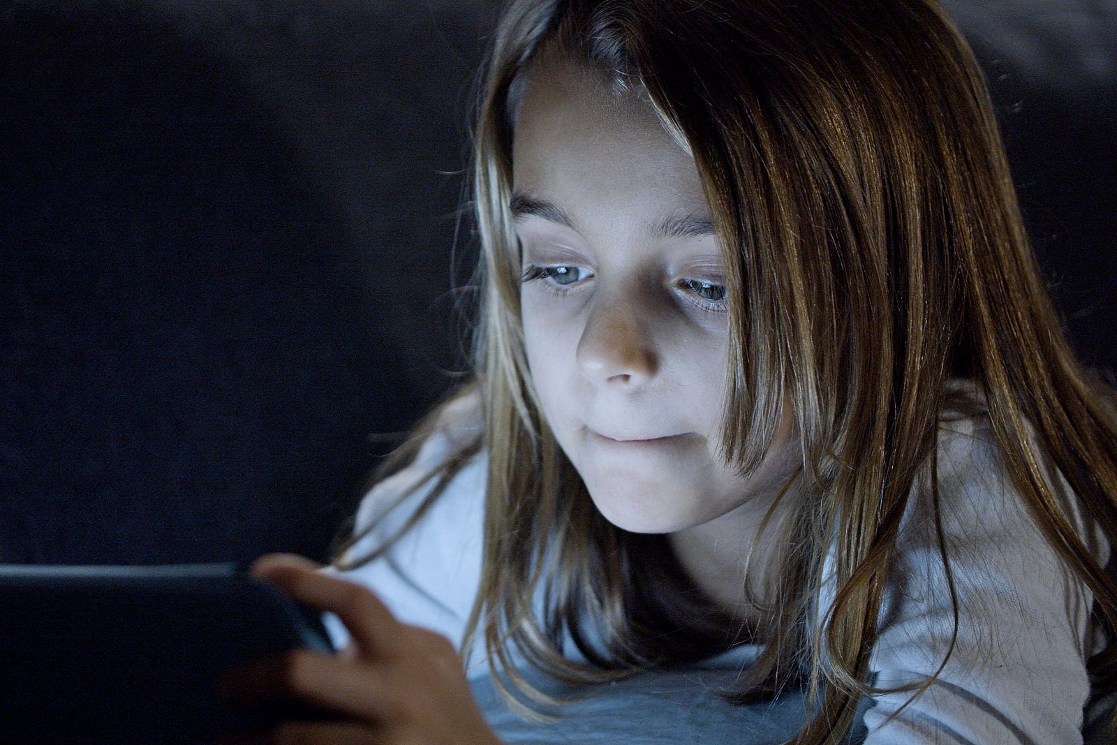 Jeune fille utilisant une tablette allongee dans la penombre